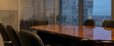 Modern corporate boardroom with conference table and chairs overlooking a city skyline through large windows.