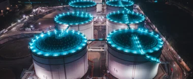 Aerial view of illuminated oil and gas storage tanks at an industrial energy facility at night, representing critical infrastructure.