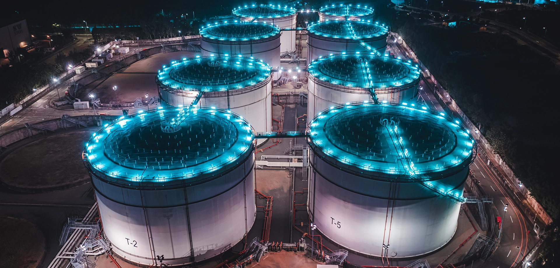Aerial view of illuminated oil and gas storage tanks at an industrial energy facility at night, representing critical infrastructure.