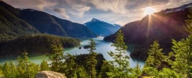 Mountain lake surrounded by evergreen forest and snow-capped peaks at sunrise, representing natural landscape and environmental resources.