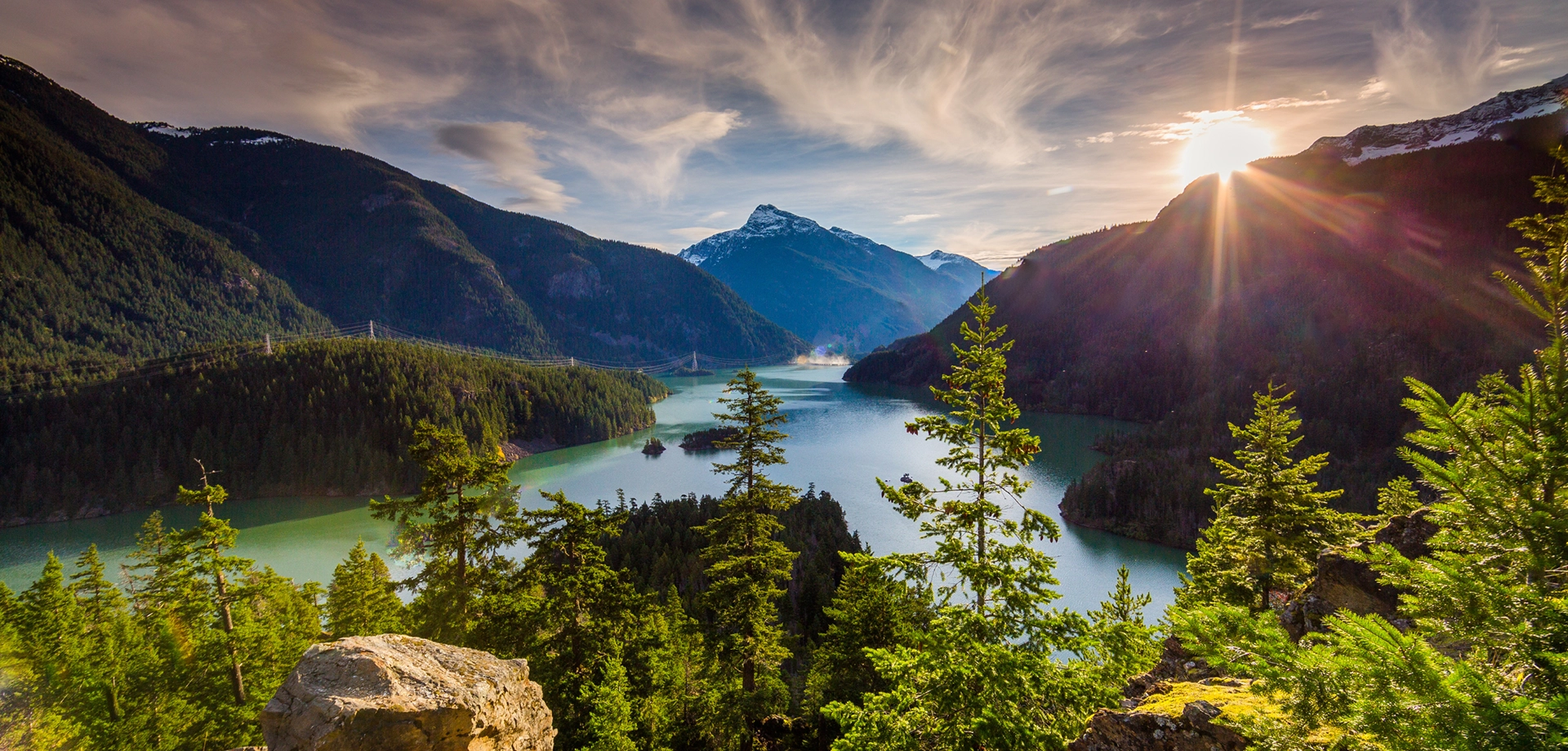Mountain lake surrounded by evergreen forest and snow-capped peaks at sunrise, representing natural landscape and environmental resources.