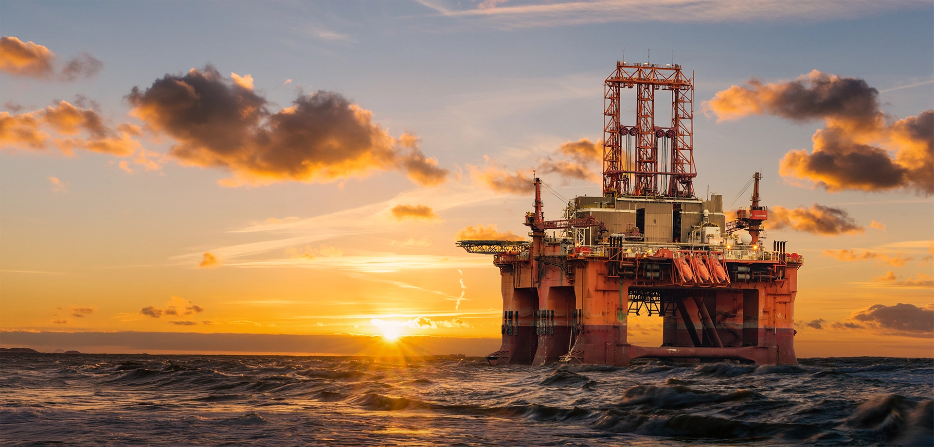 Offshore oil and gas platform at sunset over the ocean, representing energy production and critical infrastructure.